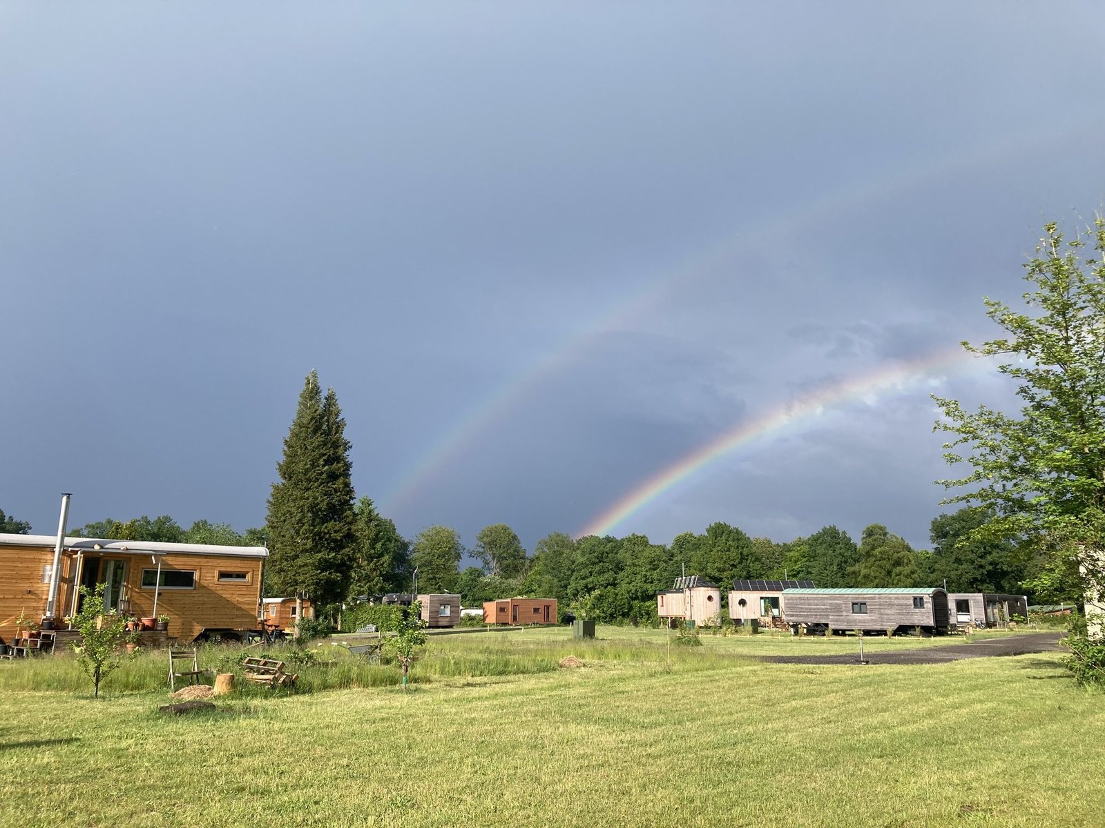 Ein doppelter Regenbogen über der Siedlung, Tiny Houses am Rand einer weiten Wiese