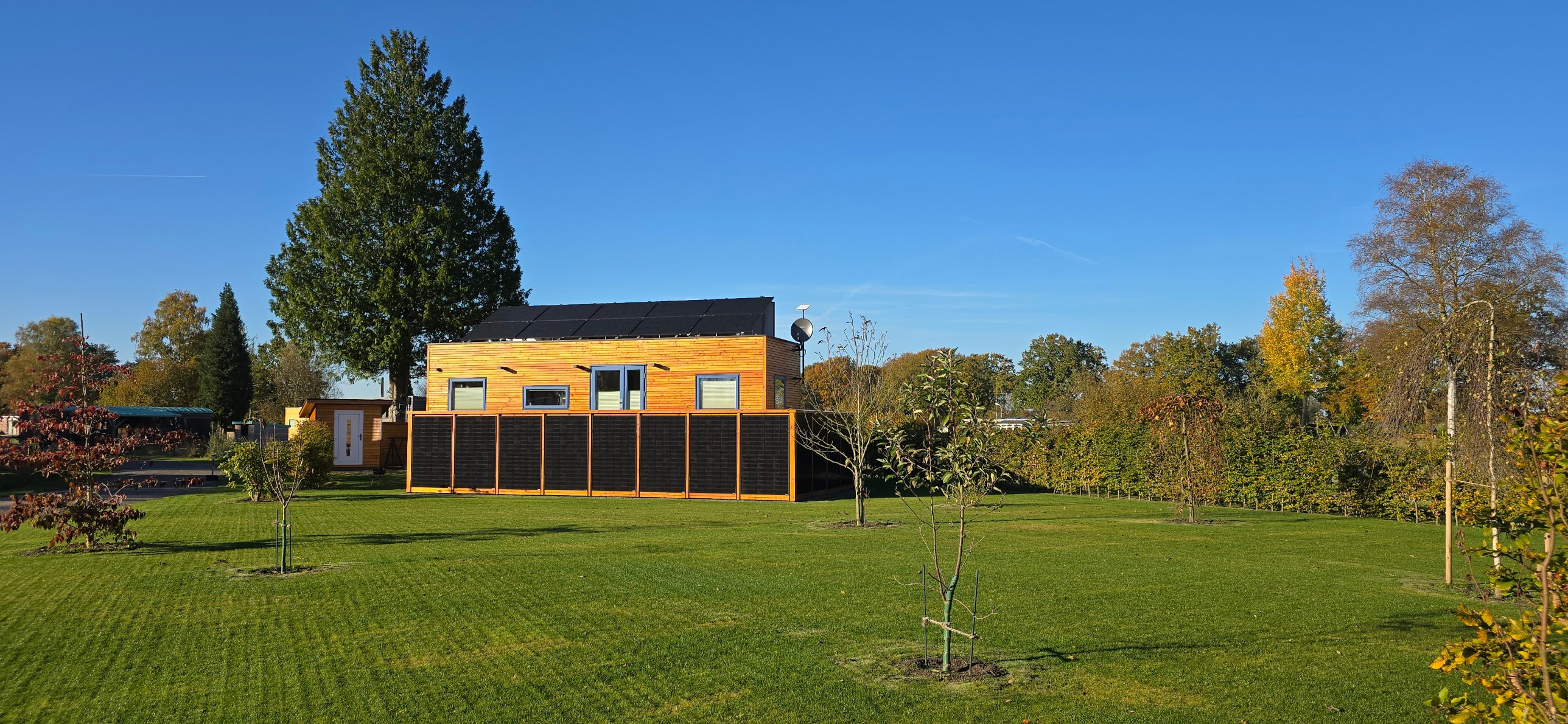 Tiny House mit Holzfassade und Solardach auf einem großzügigen Stellplatz in der Gemeinschaft, umgeben von Bäumen