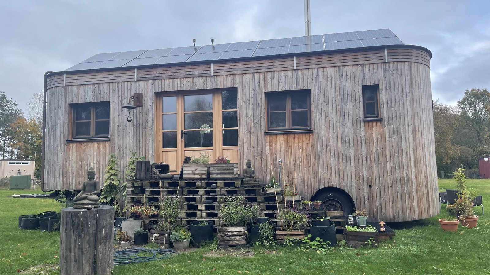 Ein Tiny House aus Holz mit Topfpflanzen und einem kleinen Garten davor